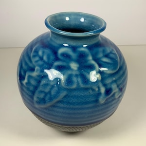 May include: A blue ceramic vase with a floral design. The vase has a textured surface and a round shape.
