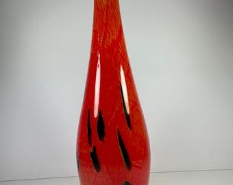 May include: A tall, teardrop-shaped glass vase. The vase is primarily red with black teardrop-shaped accents. The top of the vase has a yellow and orange pattern. The vase is a decorative item.