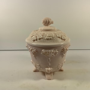May include: A pink glass candy dish with a grapevine design and three legs. The lid has a grape cluster design.