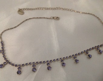 May include: Silver-toned necklace with a delicate chain and a series of small, round, lavender-colored gemstones. The necklace features a row of gemstones along the main chain and dangling gemstones. A small tag is attached.