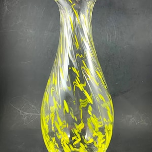 May include: A clear glass vase with a yellow swirl design. The vase has a wide mouth and a narrow base.