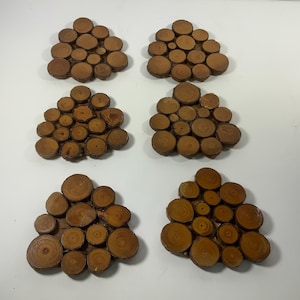 May include: Six wooden coasters, each composed of small, circular wood slices arranged in a cluster. The coasters have a natural, light brown color, showcasing the wood grain. These coasters are ideal for protecting surfaces from drink rings.