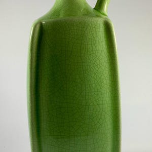May include: A green ceramic pitcher with a square body and a curved handle. The pitcher has a textured, crackled surface and a small spout. The pitcher is a light green color.