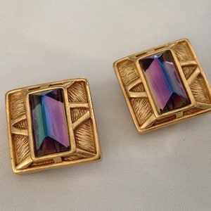 May include: A pair of gold-tone clip-on earrings with iridescent purple rectangular stones set in a geometric design.