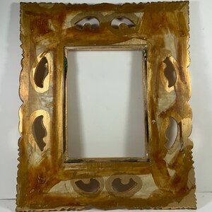 May include: A rectangular picture frame with an ornate design and a distressed gold finish. The frame has decorative cutouts and a scalloped edge. The inner opening is a simple rectangle. The frame has a vintage, antique aesthetic, suitable for a photograph or artwork.