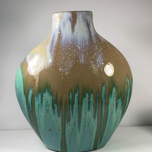May include: A large, decorative ceramic vase with a wide, rounded body and a narrow neck. The vase features a brown glaze on the upper portion, transitioning to a teal and green glaze that drips down the sides. The vase has a glossy finish.