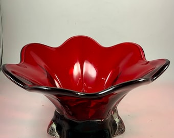 May include: A red glass bowl with a scalloped rim and a flared base. The bowl is made of clear glass with a red tint.