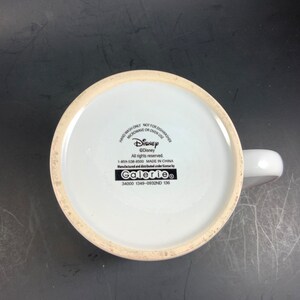 May include: White ceramic mug with a handle, featuring the Disney logo and text. The bottom of the mug displays the Disney copyright information, manufacturing details, and the Galerie brand. The mug is designed for hand washing only and is not suitable for microwave or oven use.