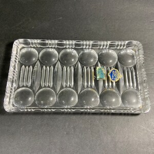 May include: Rectangular clear glass tray with a decorative pattern of circles and vertical lines. The tray has a textured border and two small blue and white labels. A vintage piece for serving or display.