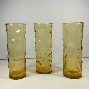 May include: Three amber glass drinking glasses with a textured surface.