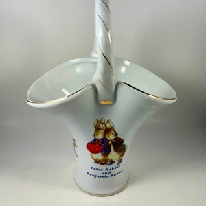 May include: White porcelain basket with a gold trim and a handle. The basket features a picture of Peter Rabbit and Benjamin Bunny.