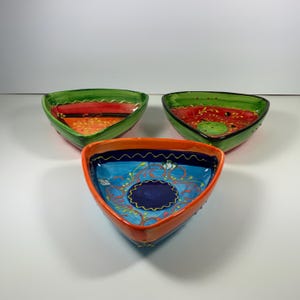 May include: Three triangular ceramic bowls with hand-painted designs. The bowls are green, blue, and orange with intricate floral patterns.