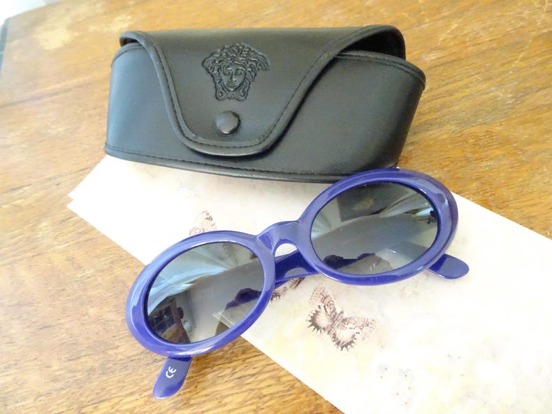 Puede incluir: Gafas de sol ovaladas con montura de pl&aacute;stico azul oscuro brillante y lentes tintadas oscuras, acompa&ntilde;adas de un estuche r&iacute;gido de cuero sint&eacute;tico negro con el logotipo de la cabeza de Medusa en relieve y cierre de bot&oacute;n a presi&oacute;n.