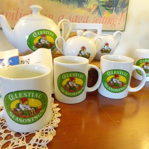May include: A white Celestial Seasonings tea set, including a teapot, creamer, sugar bowl, and mugs. Each piece features the Celestial Seasonings logo in a green oval. The set is arranged on a wooden surface.