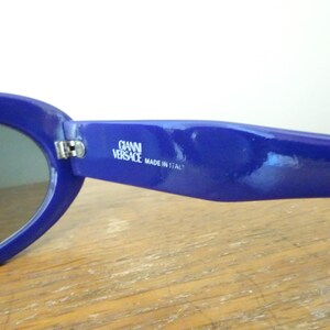Puede incluir: Un par de gafas de sol azul real con monturas ovaladas. La patilla interior presenta el texto impreso en blanco GIANNI VERSACE MADE IN ITALY. Las gafas tienen un acabado brillante y una bisagra met&aacute;lica que une la montura a la patilla.