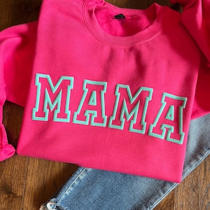May include: A pink sweatshirt with the word "MAMA" in teal green letters.