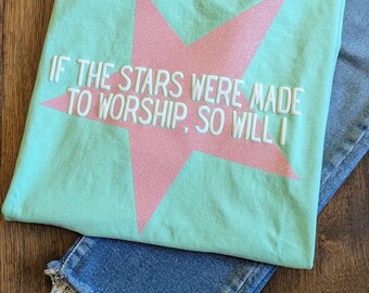 May include: A mint green short-sleeve t-shirt featuring a large pink glitter star graphic centered on the chest. The text "IF THE STARS WERE MADE TO WORSHIP, SO WILL I" is printed in white across the star. The shirt has a crew neckline and a Comfort Colors brand label.
