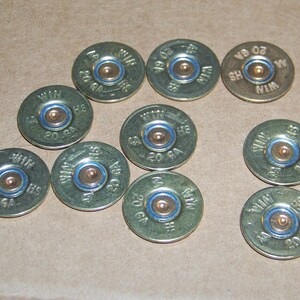 May include: Ten gold shotgun shells with blue trim. Each shell is labeled "WIN 20 GA" and has a small, round, copper-colored center.