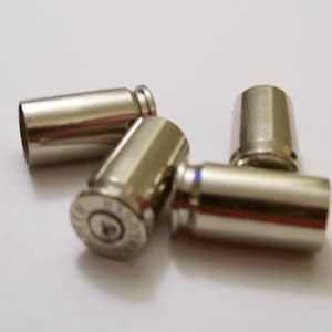 May include: Four shiny, metallic bullet casings are arranged on a white surface. The casings have a cylindrical shape with a slightly tapered end and a circular base. The casings are silver in color and reflect light.