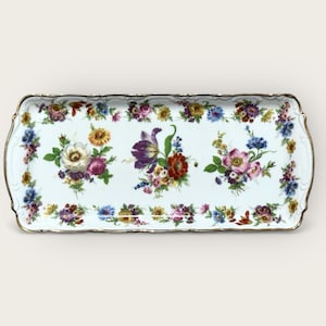 May include: Rectangular porcelain serving tray with a white background and a gold rim. The tray is decorated with colorful floral arrangements in the center and along the edges. The flowers include roses, tulips, and other blooms.