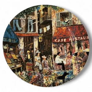 May include: Decorative round plate featuring a colorful illustration of a European street scene with a cafe, shops, and people. The plate has a white background and a glossy finish. The words "CAFE RESTAURANT" are visible.