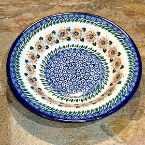 May include: A ceramic bowl with a blue rim and a white interior. The bowl is decorated with orange floral patterns, green leaf designs, and a blue floral center. The bowl is approximately 9 inches in diameter.