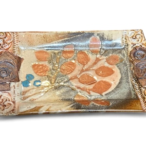 May include: Rectangular ceramic serving dish with a leaf design. The dish features a beige background with orange leaves and blue accents. The edges have decorative brown and gold accents, including embossed circular designs.