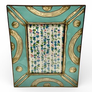 Puede incluir: Un marco de fotos turquesa con detalles dorados. El marco tiene un inserto con estampado floral. El marco tiene forma cuadrada con bordes redondeados y dise&ntilde;os dorados decorativos. Es un art&iacute;culo decorativo.