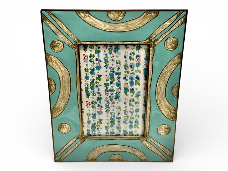 Puede incluir: Un marco de fotos turquesa con detalles dorados. El marco tiene un inserto con estampado floral. El marco tiene forma cuadrada con bordes redondeados y dise&ntilde;os dorados decorativos. Es un art&iacute;culo decorativo.