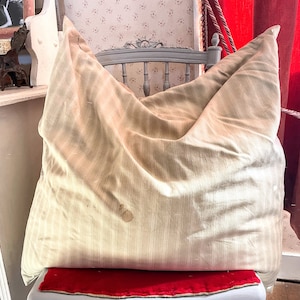 Peut inclure: Un grand coussin beige à fines rayures brun clair posé sur une chaise avec un coussin rouge. Le coussin est légèrement froissé et présente une tache brune.