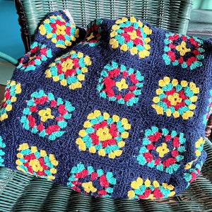 May include: A crocheted blanket with a navy blue background and colorful granny squares in red, yellow, and green.