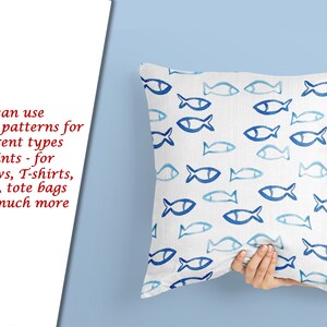 May include: A white pillow with a blue and white fish pattern. The pillow is being held by a hand.