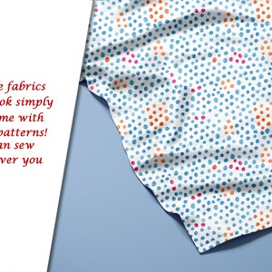 May include: A white fabric with a repeating pattern of blue, orange, and pink polka dots. The fabric is folded and draped over a blue surface.