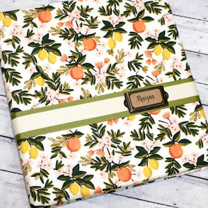 May include: A white recipe binder with a green and white floral pattern featuring lemons and oranges. The binder has a green ribbon and a brown label that says "Recipes".