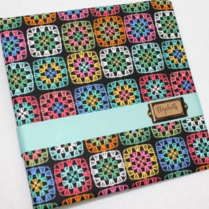 May include: A black scrapbook with a colorful crocheted pattern and a brown name tag that says "Elizabeth".