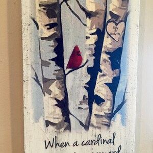 Puede incluir: Un letrero de madera con una imagen pintada de tres abedules y un cardenal rojo. El letrero tiene el texto "Cuando un cardenal aparece en tu jard&iacute;n, es un visitante del cielo." y un coraz&oacute;n con los nombres "Roy & Roberta" en &eacute;l.
