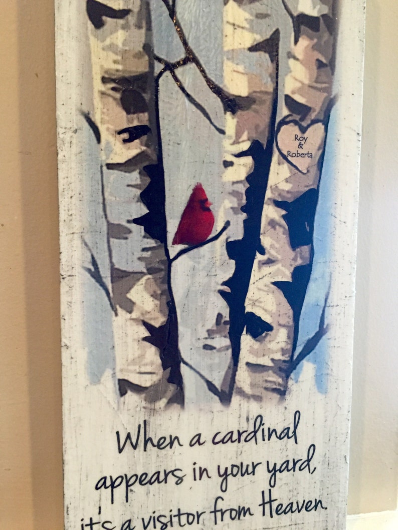Puede incluir: Un letrero de madera con una imagen pintada de tres abedules y un cardenal rojo. El letrero tiene el texto "Cuando un cardenal aparece en tu jard&iacute;n, es un visitante del cielo." y un coraz&oacute;n con los nombres "Roy & Roberta" en &eacute;l.