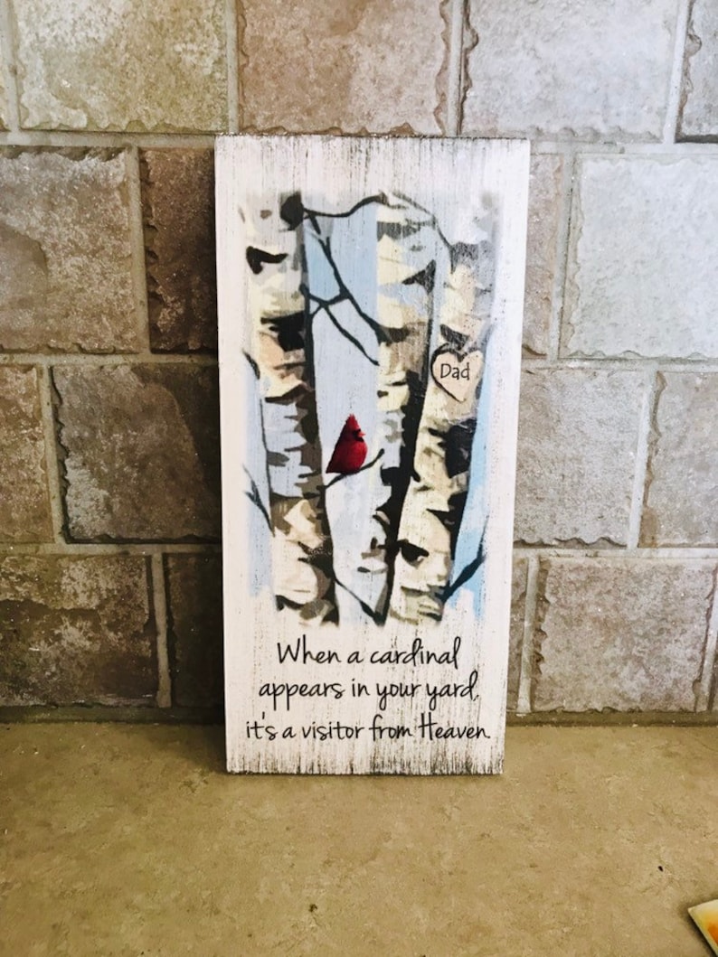 Puede incluir: Un letrero de madera con una imagen pintada de abedules y un cardenal rojo. El letrero tiene el texto "Pap&aacute;" en forma de coraz&oacute;n y el texto "Cuando un cardenal aparece en tu jard&iacute;n, es un visitante del cielo."