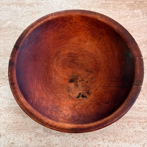 May include: A round, deep wooden bowl with a rich, dark reddish-brown finish. The surface displays visible wood grain patterns, natural texture, and a distinct horizontal crack extending from the right edge toward the center of the basin.
