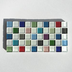 May include: A rectangular mosaic tile sheet featuring small, square tiles in a variety of colours, such as blue, green, red, and white. The tiles are arranged in a grid pattern, creating a visually appealing design. The mosaic is set against a white background.