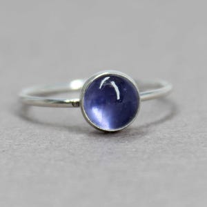 May include: A silver ring with a round, cabochon-cut, purple gemstone.