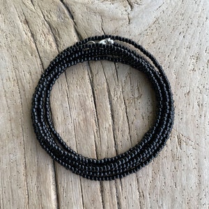May include: A black beaded choker necklace with a silver clasp. The necklace is made of small, round beads and is layered for a thicker look.