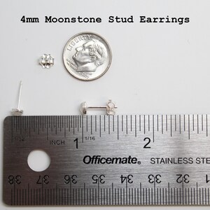 May include: A pair of silver stud earrings with 4mm moonstone gemstones. The earrings are shown next to a ruler for size comparison. The ruler is marked in inches.