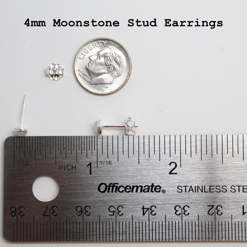 May include: A pair of silver stud earrings with 4mm moonstone gemstones. The earrings are shown next to a ruler for size comparison. The ruler is marked in inches.
