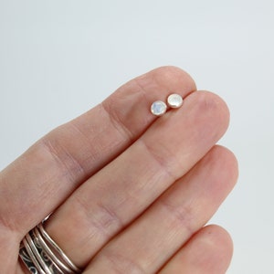 May include: A pair of silver stud earrings with small round moonstone gemstones.