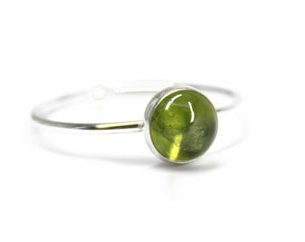 May include: A silver ring featuring a green gemstone. The ring is a simple band with a round, cabochon-cut stone.