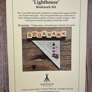 May include: A 'Lighthouse' Bookmark Kit. The kit includes vintage paper, perforated paper, threads, and a needle. The bookmark is stitched on antique book pages. The kit features a lighthouse design and the word 'BOOKMARK' spelled out with letter tiles.