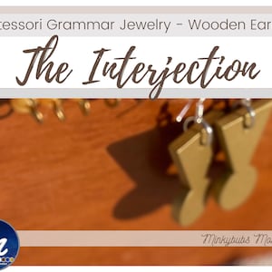 Könnte beinhalten: Hölzerne Ohrringe in Form des Interjektionssymbols, in Gold lackiert. Die Ohrringe hängen an einer Holzoberfläche. Der Text "The Interjection" ist in braunen Kursivbuchstaben über den Ohrringen geschrieben.