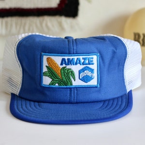May include: A blue and white trucker hat with a patch featuring a corn cob and the text "AMAZE MOBAY".