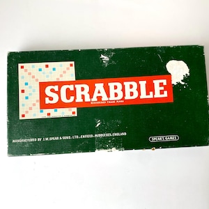 May include: A green box with the word "SCRABBLE" in red letters and a small image of a game board. The box is labeled "Manufactured by J.W. Spear & Sons, Ltd. Enfield, Middlesex, England" and "Spear's Games".